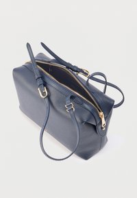 Δερμάτινη τσάντα χειρός σε ναυτικό μπλε με χρυστό φερμουάρ, ρυθμιζόμενους ιμάντες και ημι-ανοιχτή κύρια θήκη που αποκαλύπτει σκοτεινό εσωτερικό.