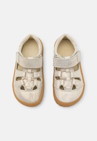 Barefoot-sko med metallisk lys gullfarge på overflaten, åpen design med utskjæringer, borrelås-stropp og brun gummisåle. Mykt teksturert innvendig fôr.