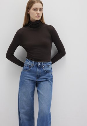 Enganliegendes schwarzes Rollkragenoberteil, kombiniert mit hoch taillierten, hellblauen Jeans aus Denim, die über rohe Säume und ein Fünf-Taschen-Design verfügen. Glatte Texturen.