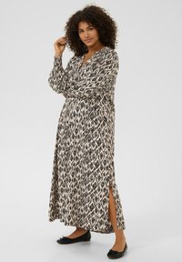 Robe longue à motifs en noir et crème, avec un décolleté en V, des manches longues et des fentes sur les côtés. Associée à des ballerines noires pour le contraste.
