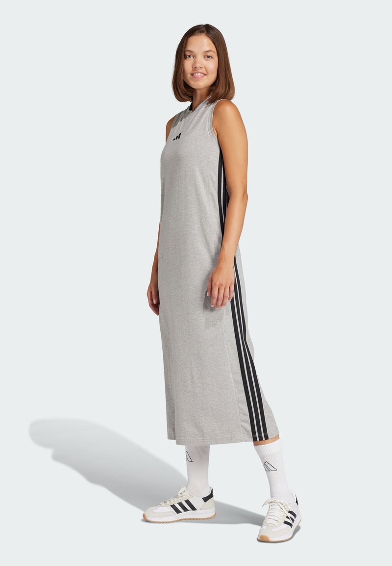 Siva halter haljina s bočnim crnim prugama, napravljena od mekog materijala. Uparena s bijelim čarapama i crno-bijelim tenisicama.
