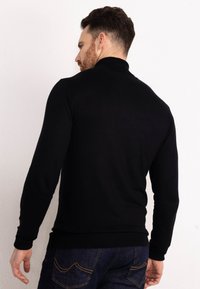 Maglione nero a collo alto con maniche lunghe, dalla texture liscia, con polsini e orlo a costine, abbinato a jeans blu scuro con cuciture distintive sulle tasche.
