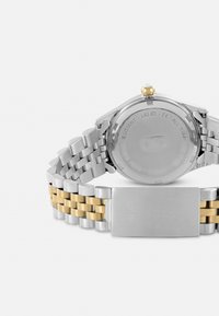 Silber- und goldfarbene Zweiton-Uhr aus Metall mit einem Edelstahlarmband, rundem Gehäuse und einer goldenen Krone. Die Rückseite ist mit Markendetails graviert.