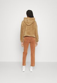 Hoodie corto marrone e peloso con cappuccio; abbinato a pantaloni rustici a vita alta e a gamba affusolata; sneakers bianche con finitura testurizzata.