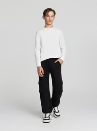 Biała koszula z długim rękawem w połączeniu z czarnymi spodniami cargo z dużymi bocznymi kieszeniami. Całość dopełniają czarno-białe trampki.