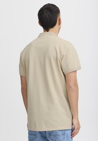 Beige pólóing puha, texturált anyagból, klasszikus gallérral és rövid ujjakkal, egyenes szegéllyel és látható logók nélkül.