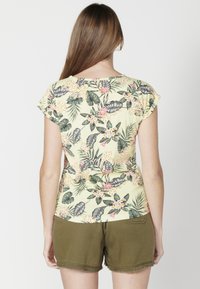Koszulka z krótkim rękawem w żółty kwiatowy wzór z zielonymi liśćmi i różowymi akcentami, połączona z oliwkowymi szortami z postrzępionym dołem.