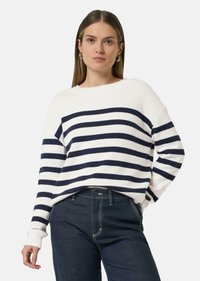Witte trui met marineblauwe horizontale strepen, geribde manchetten en een ontspannen pasvorm. Gepaard met donkere denim jeans, met contrasterende stiksels.