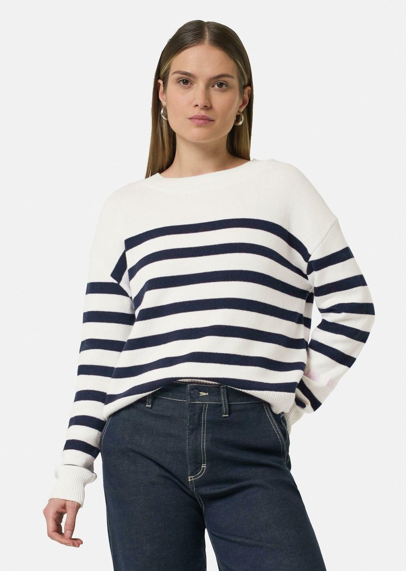 Witte trui met marineblauwe horizontale strepen, geribde manchetten en een ontspannen pasvorm. Gepaard met donkere denim jeans, met contrasterende stiksels.