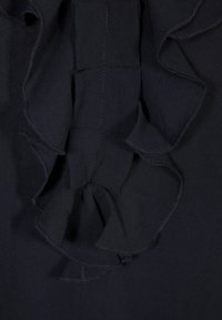 Svart tyg topp med en volangdetalj som löper vertikalt ner i mitten. Mjuk textur och fin sömnad längs kanterna.