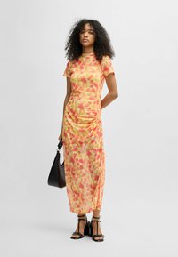 Fitted short-sleeve dress in yellow with red and orange floral pattern. Features ruched sides, high collar, and a mid-length design.