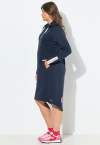 Abito a cappuccio navy con maniche lunghe, tasche laterali e dettagli rosa. Realizzato in materiale morbido, presenta un orlo leggermente curvo e un dettaglio con logo.