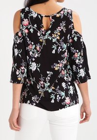 Top floreale nero con design spalle scoperte, maniche corte e schiena a occhiello. Tessuto sovrapposto con motivi di fiori multicolori.