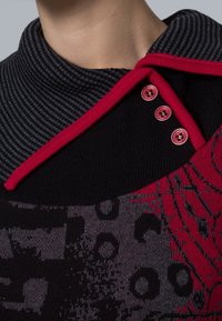 Närbild av en svart och röd mönstrad tröja med en randig krage, röd kant och tre röda knappar nära halslinningen.