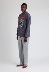 Camisa de manga larga gris que presenta un gráfico colorido de Star Wars. Combinada con pantalones grises de un patrón. Tejido suave con un corte relajado.