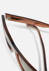 Ochelari de soare din material bio-based maro, cu un finisaj lucios, având un design elegant și lentile colorate. Accesorii reflective la balama.