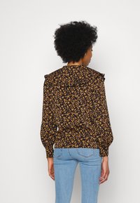 Blusa preta floral com padrões em amarelo e laranja, ombros franzidos e mangas longas, combinada com jeans azul claro.