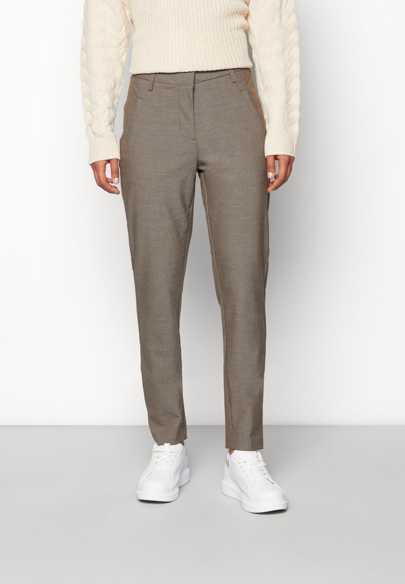 Pantalon beige sur mesure avec une finition texturée, doté de poches latérales et d'une coupe slim, associé à des baskets blanches de sport.