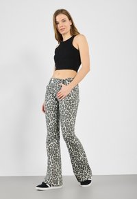 Bredde bukser med leopardmønster i grå og svart denim, kombinert med en tettsittende, svart ribbestrikket crop-top og svarte joggesko.
