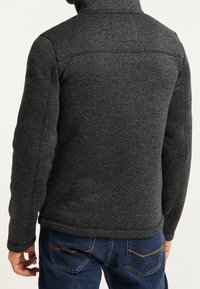 Tmavě šedá fleecová bunda s kapucí a texturovaným povrchem. Má přiléhavý střih a kontrastní prošití v oblasti pasu. Minimální množství kovových doplňků.