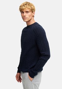 Granatowy sweter w warkoczowy splot z okrągłym dekoltem, teksturowanym wzorem, ściągaczami przy mankietach i u dołu, oraz dopasowaną sylwetką.