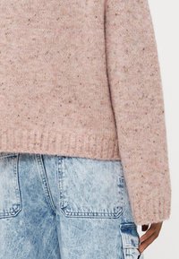 Svetlo roza pleteni pulover z teksturirano površino. Rebrast rob in manšete. Pairs with bledimi modrimi denim cargo hlačami z žepi za zakrpavanje.