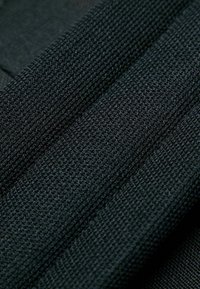 Schwarzer strukturierter Stoff mit einem gerippten Muster, das aus charakteristischen Linien und unterschiedlichen Dicken besteht. Weiches, gewebtes Material mit matter Oberfläche.