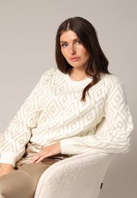 Pull crème avec un motif de losanges en relief, des poignets côtelés et un col rond, porté sur un pantalon texturé beige. Matière en tricot douce.