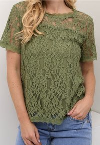 Haut en dentelle verte à motif floral, manches courtes, encolure festonnée et texture douce, assorti à un jean en denim bleu clair.