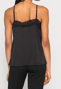 Camisola nera con bordo in pizzo sul collo, spalline regolabili e vestibilità ampia. Realizzata in tessuto morbido con una finitura liscia.