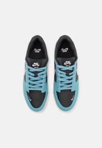 Tênis Nike SB com parte superior em couro turquesa e preto, caixa de dedo perfurada, detalhes em rosa e atacadores pretos. Sola branca com logótipo.