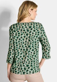 Groene luipaardprint blouse met 3/4 mouwen, met een relaxte pasvorm, zachte textuur en contrasterende beige accenten langs de halslijn.