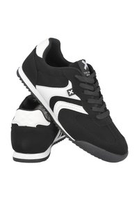 Zapatillas deportivas en blanco y negro con una parte superior sintética lisa, cierre de cordones, suela texturizada y un diseño de acento lateral distintivo.