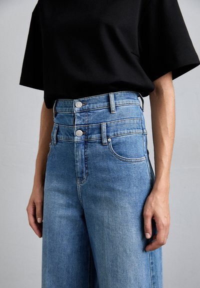 Magas derekú, világoskék farmernadrág dupla gombos záródással, széles lábakkal és enyhe kopással, fekete, rövid ujjú topal párosítva.