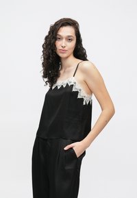Czarny satynowy top na ramiączkach z delikatną białą koronkową lamówką wzdłuż dekoltu, z regulowanymi cienkimi ramiączkami i luźnym krojem.