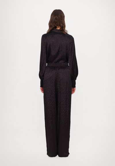 Svart, mønstrete jumpsuit med lange ermer, innsvingt liv, og en glatt tekstur, med vide bukser og krage.