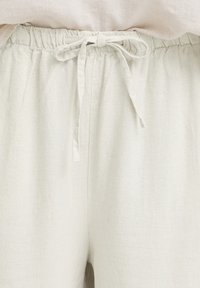 Pantalones de lino beige con cintura elástica y cordón de tela atado en la parte delantera.