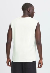 Camicia senza maniche in cotone bianco con scollatura rotonda e vestibilità morbida. Tessuto liscio, design minimalista, priva di motivi o accenti.