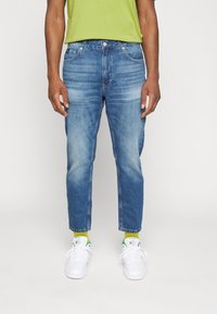 Ljusblå denimjeans med avslappnad passform, blekta detaljer och avkortade fållar. Kombineras med vita sneakers och gröna accentstrumpor.