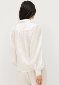 Witte linnen blouse met opgezette mouwen, geraffineerde achterkant en een klassieke kraag. Zachte, lichte stof met een gestructureerde afwerking.