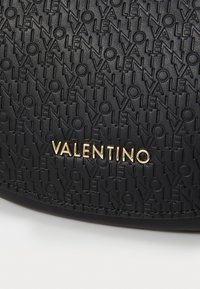 Sorte teksturert skinnveske med et preget mønster av merkevarenavnet "Valentino" og en gull logo aksent.