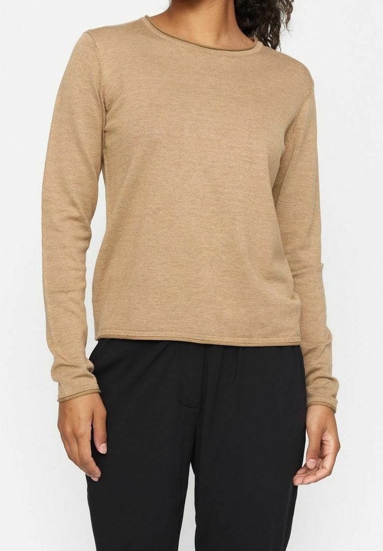 Femme portant un haut en tricot à manches longues couleur camel associé à un pantalon noir ample, debout avec les bras détendus le long du corps.