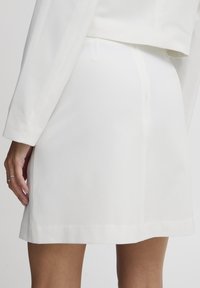 Jupe blanche avec une texture lisse, un design ajusté et des lignes épurées. Comprend une fermeture éclair discrète à l'arrière et un ourlet droit.