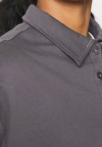 Szary polo z klasycznym kołnierzykiem, charakteryzujący się miękką teksturą i dwoma okrągłymi guzikami na listwie, wykończony białymi przeszyciami.