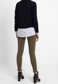 Mörk marinblå kort cardigan över en ljusblå och vit randig skjorta med små svarta detaljer, ihop med olivgröna skinny jeans och svarta klackar.