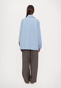 Světlounce modrá volná bunda s klopovým límcem v kombinaci s hnědými širokými kalhotami s kostkovaným vzorem. Hladká textura, bez viditelných vzorů či doplňků.