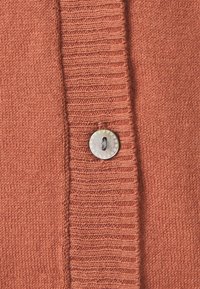 Světle rezavý pletený kardigan s knoflíkovým zapínáním a texturovaným povrchem. Viditelné žebrované a hladké části v látce.