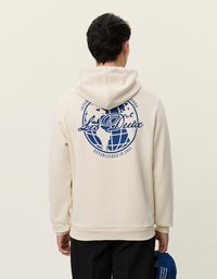 Kremowy hoodie z graficznym motywem niebieskiego globu oraz napisem na plecach. Miękka tekstura, regularny krój oraz kangurkowa kieszeń z przodu.