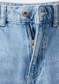 Light blue denim jeans feature a zip fly, silver rivet, and a slightly faded texture, showing stitching details and pockets.