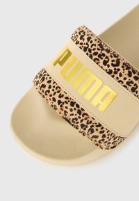 Puma-liukusissa on beige pohja ja leopardikuvioinen yläremmi, jossa on kultainen brändäys. Materiaali on sileä ja siinä on teksturoitu kuvio.